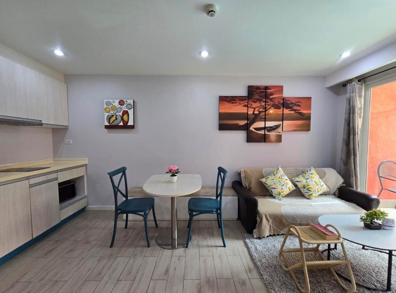 A compact living space with a kitchenette, a dining area with two chairs, a sofa with cushions, and a large window with curtains.