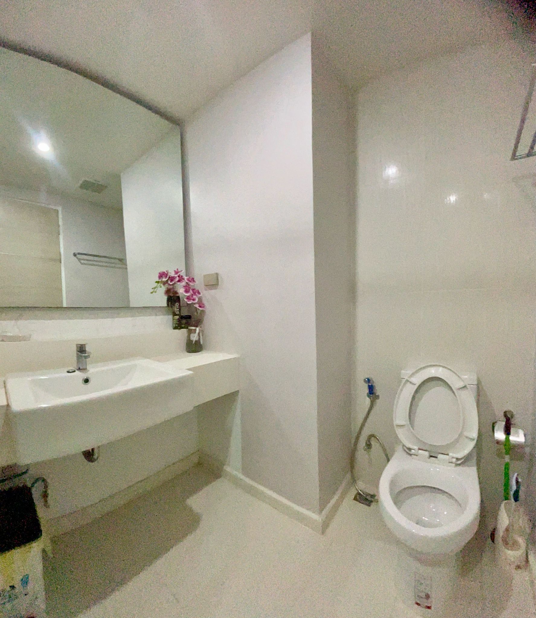 A bathroom with a white sink, mirror, toilet, and a vase with flowers.
