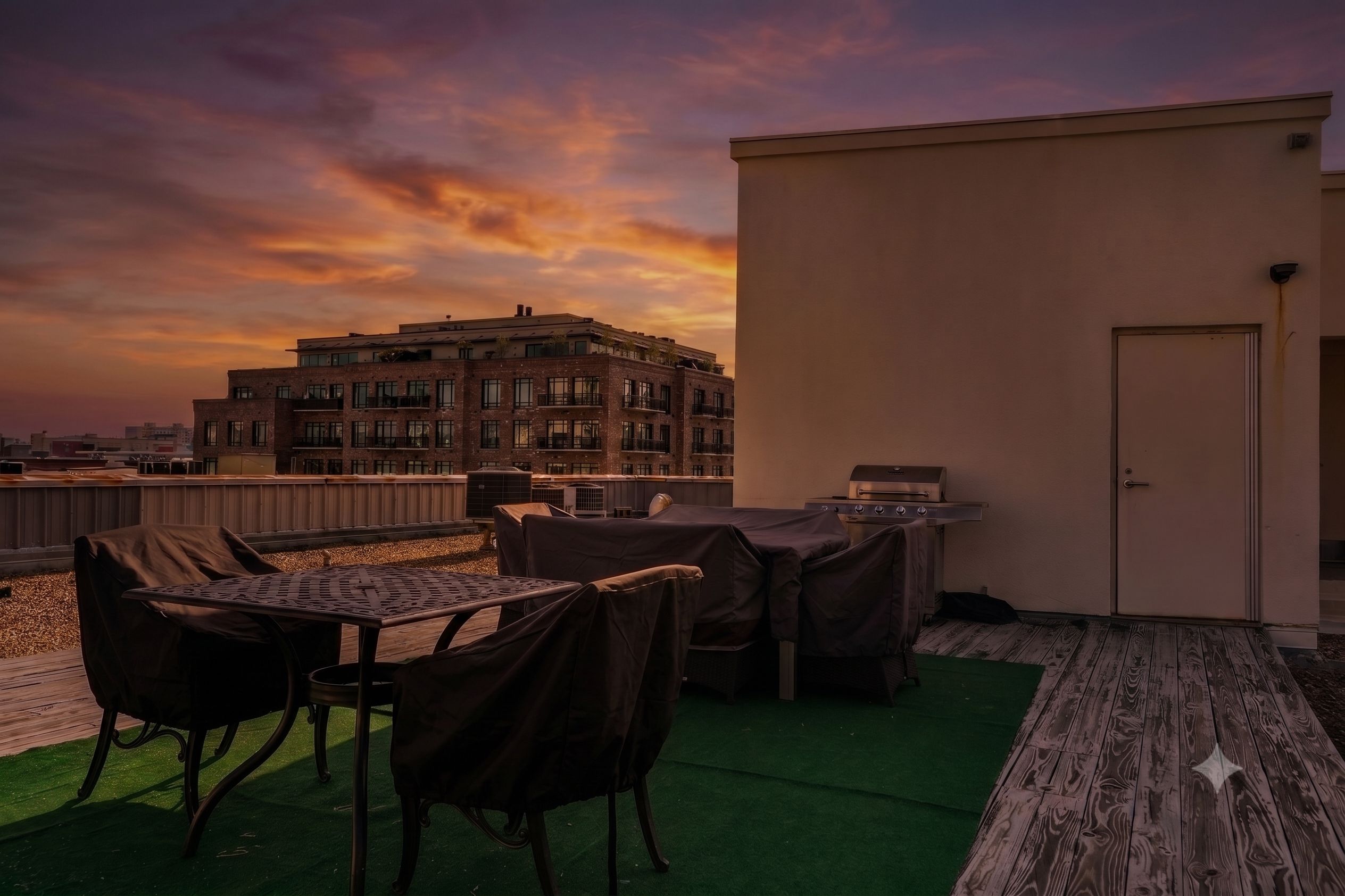 A rooftop terrace with a table and chairs, a barbecue grill, and a view of a building in the background.