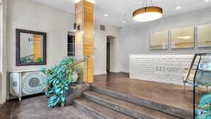 A modern reception area with a white brick wall, a wooden column, and a staircase leading to an upper floor. - Chic 1BR in Warehouse District with. King bed, exposed brick, walk to FQ (New Orleans)
