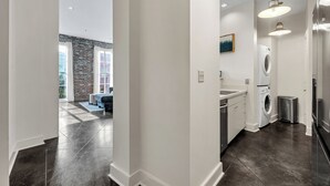 A modern kitchen with dark flooring, white cabinetry, and a built-in washing machine. - Chic 1BR in Warehouse District with. King bed, exposed brick, walk to FQ (New Orleans)