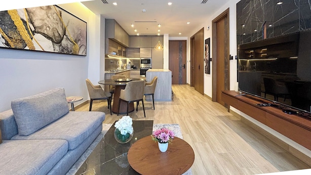 Un salon moderne avec un canapé, une table basse et un coin repas comprenant des chaises, et une cuisine en arrière-plan.