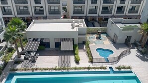 Un espace piscine aménagé sur le toit, comprenant une grande piscine, des chaises longues et un petit jacuzzi.