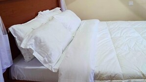 A bed with a wooden headboard, white bedding, and a white canopy. - Charming 2-bedroom house in Arusha with WiFi (Arusha)