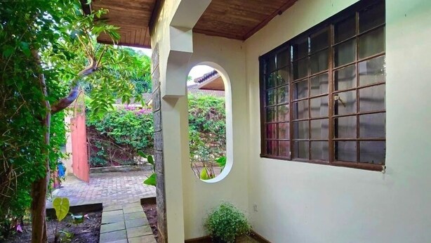 A covered outdoor area with a tiled walkway, a potted plant, and a window with bars. - Charming 2-bedroom house in Arusha with WiFi (Arusha)