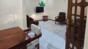 A spacious living room with a wooden dining table, two armchairs, a small coffee table, and a TV mounted on the wall. - Charming 2-bedroom house in Arusha with WiFi (Arusha)