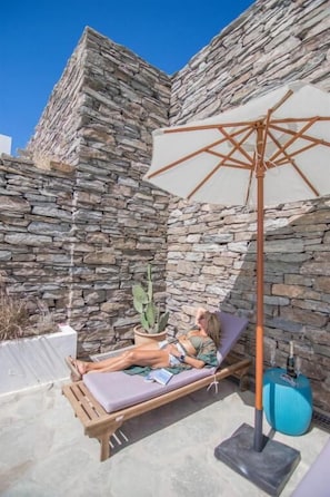 Relax in a serene outdoor space with a stone wall backdrop, a comfortable lounge chair, and soothing ambiance.