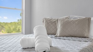 A neatly made bed with a quilted white comforter and two pillows, a window with a view of greenery, and a white wall. - Book your Labor Day stay before dates fill up / Plus Free Night! (Kissimmee)
