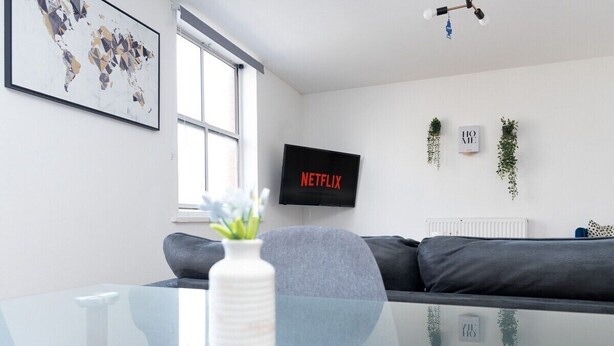 Un salon moderne avec une table basse en verre, un canapé gris et un téléviseur affichant le logo « NETFLIX ».