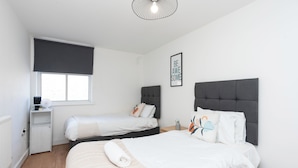 Une chambre avec deux lits, une petite table de chevet, un radiateur et une fenêtre avec un store enrouleur.