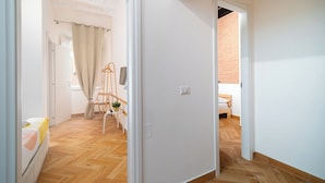 A bedroom with a wooden floor, a bed, a chair, a TV, and a window with curtains. - La Posada by Rentbeat (Civitavecchia)