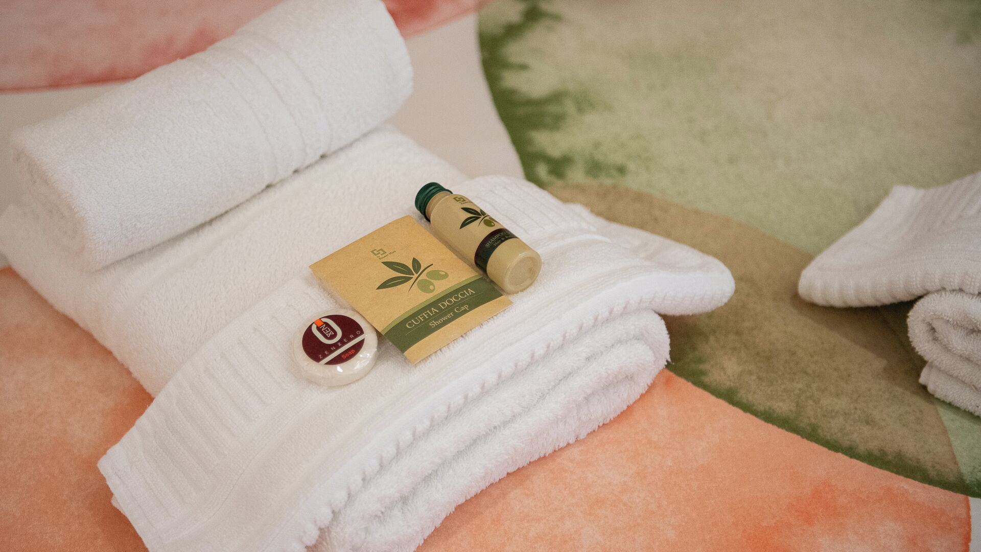 Une serviette blanche soigneusement pliée, avec un bonnet de douche et un petit flacon de savon posés dessus.
