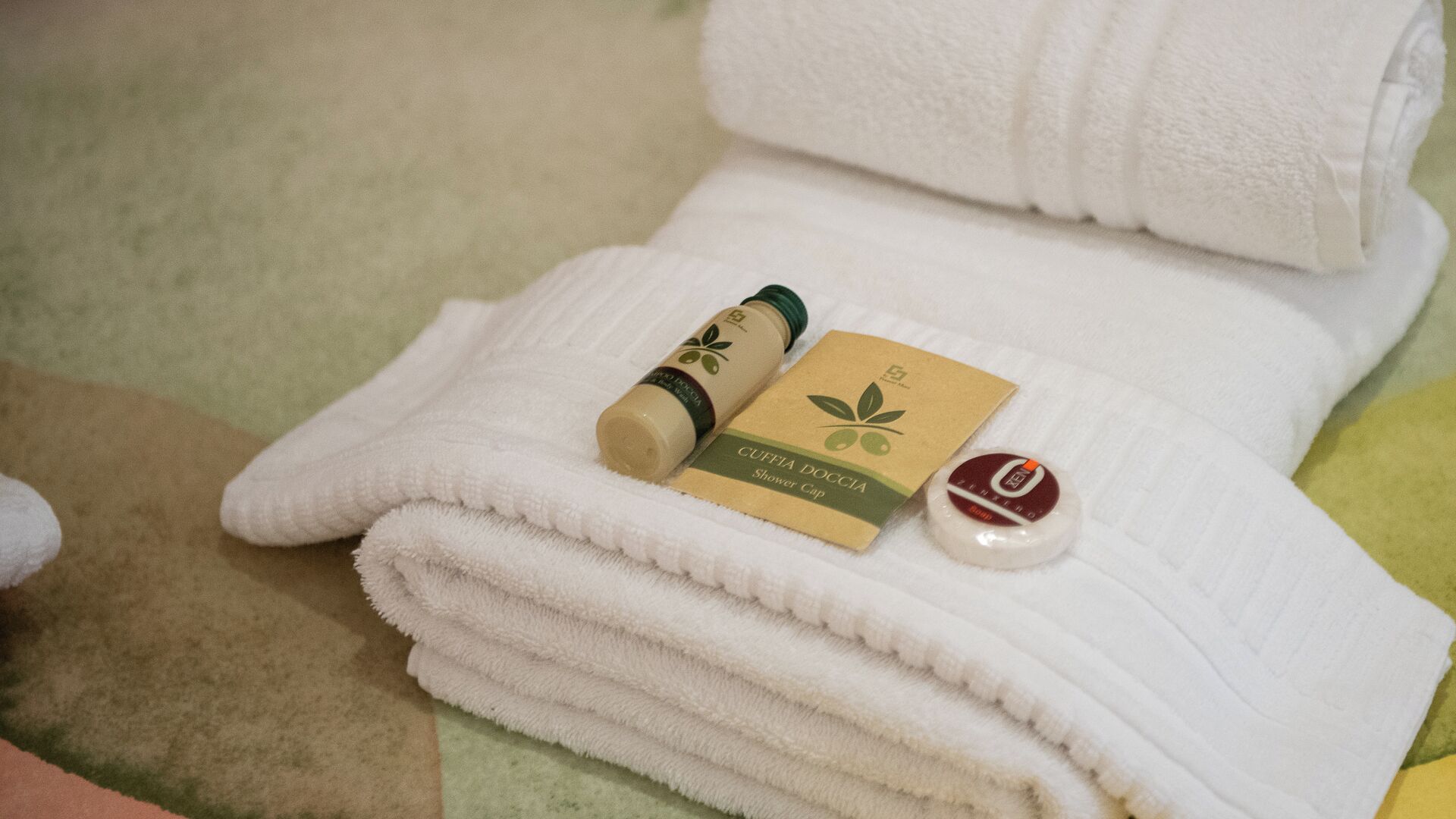 A neatly folded white towel with a bottle of shower gel and a cap on top.