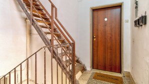 A wooden door with a brass doorknob, a metal staircase with a metal railing, and a welcome mat at the base of the stairs. - La Posada by Rentbeat (Civitavecchia)