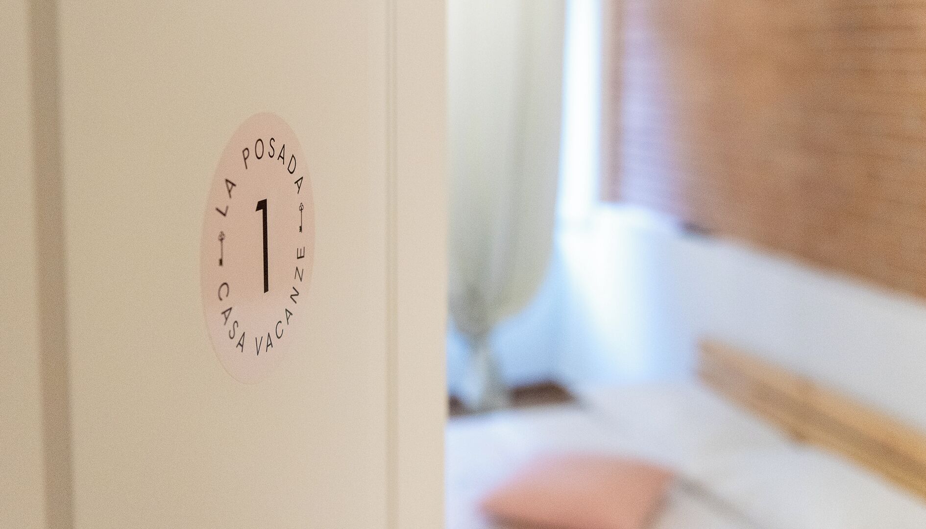 Una puerta con un adhesivo circular que dice "POSADA 1" y "CASA DE VACANZE", indicando un número de habitación y una casa de vacaciones.