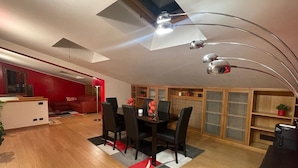 A modern living room with a dining area, featuring a wooden floor, a red sofa, a dining table with chairs, and a ceiling with skylights and track lighting. - Paradise home (Rome)
