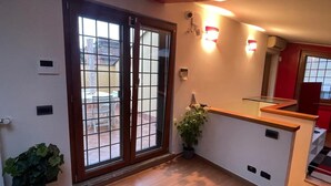 A room with a sliding glass door leading to an outdoor area, a small reception desk, and a potted plant. - Paradise home (Rome)