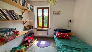 A small, well-organized room with a bed, a desk with books and puzzles, a window with curtains, and a radiator. - Charming traditional farmhouse, relaxation and nature (Taintrux)
