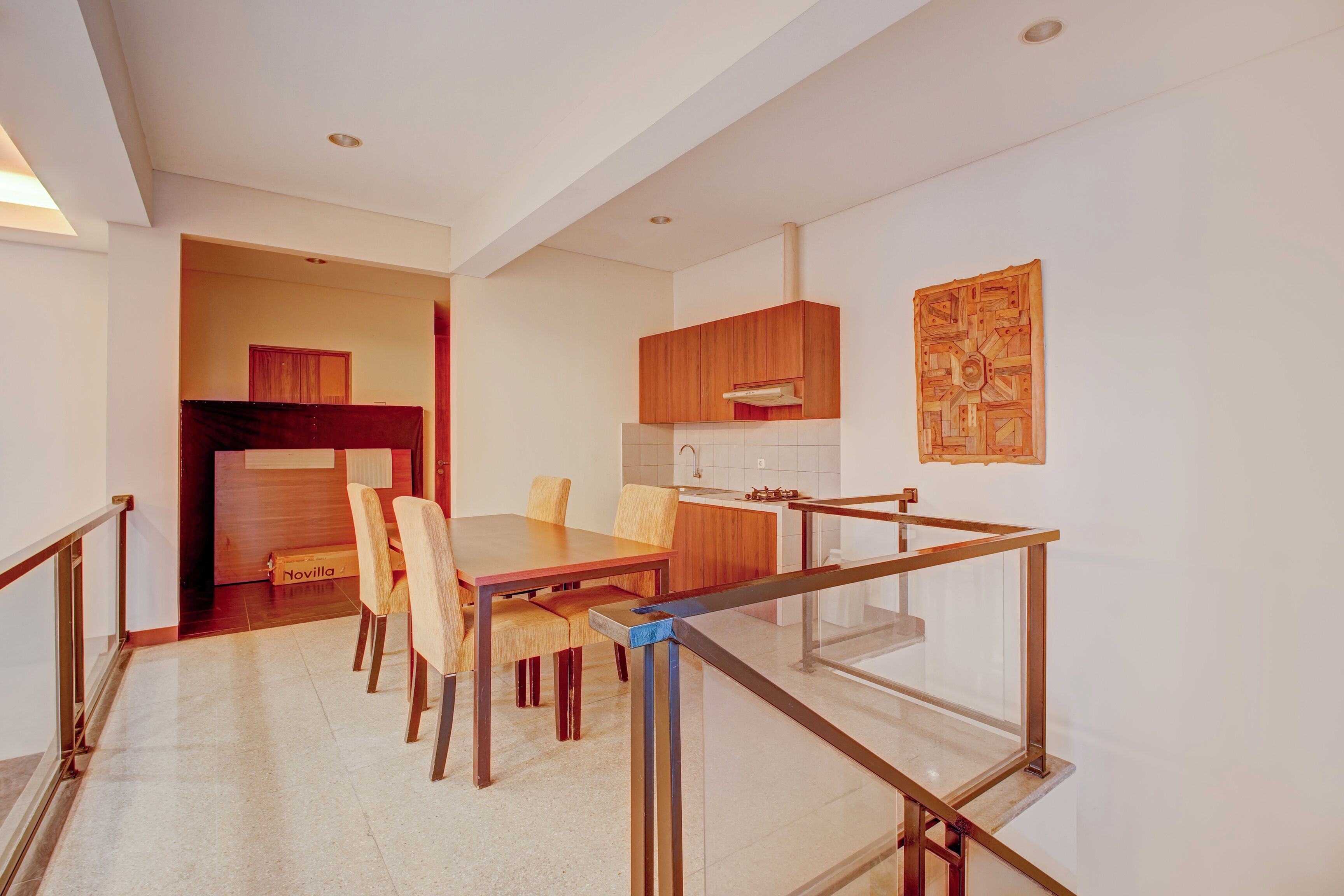 A modern kitchen with wooden cabinets, a dining area with a glass railing, and a visible artwork on the wall.
