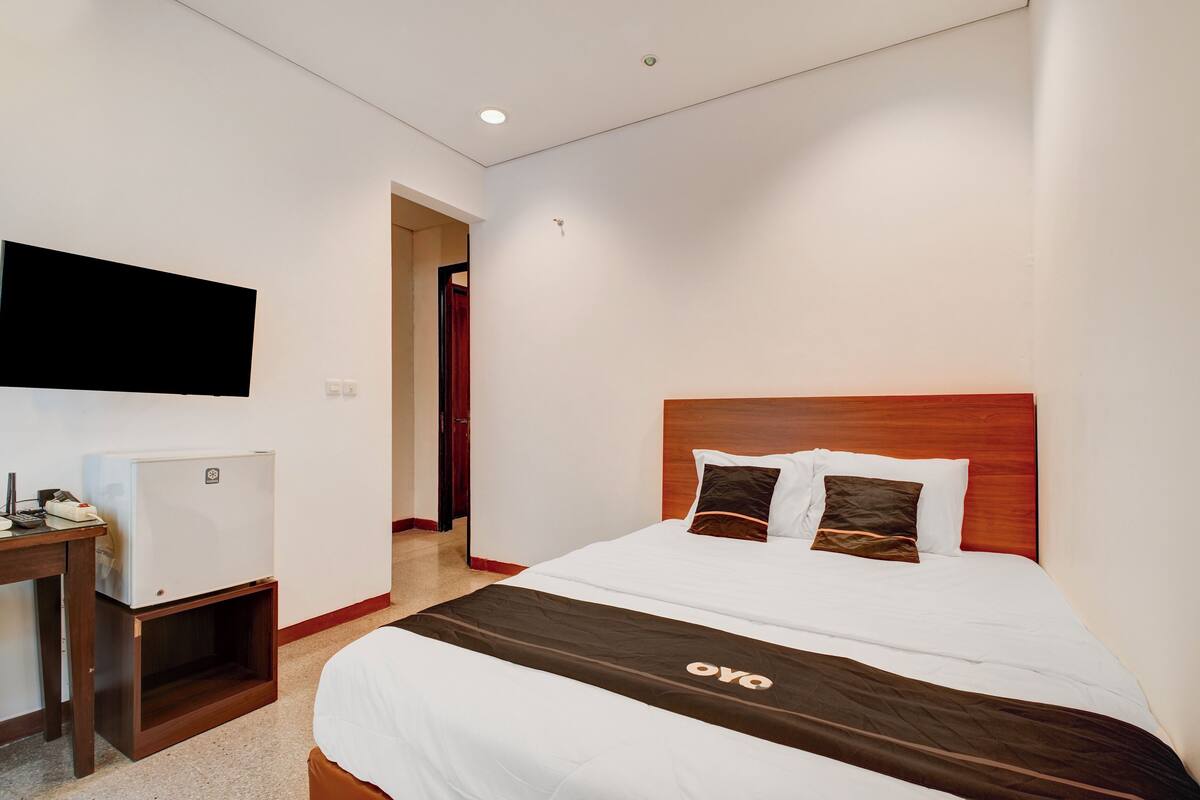A hotel room with a bed, a TV mounted on the wall, and a small table with a refrigerator.
