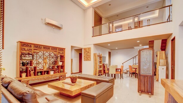 A spacious living area with a high ceiling, a wooden coffee table, a leather sofa, and a dining area with chairs and a table. - Collection O near MRT Cipete Raya formerly Terogong Sembilan (Jakarta)