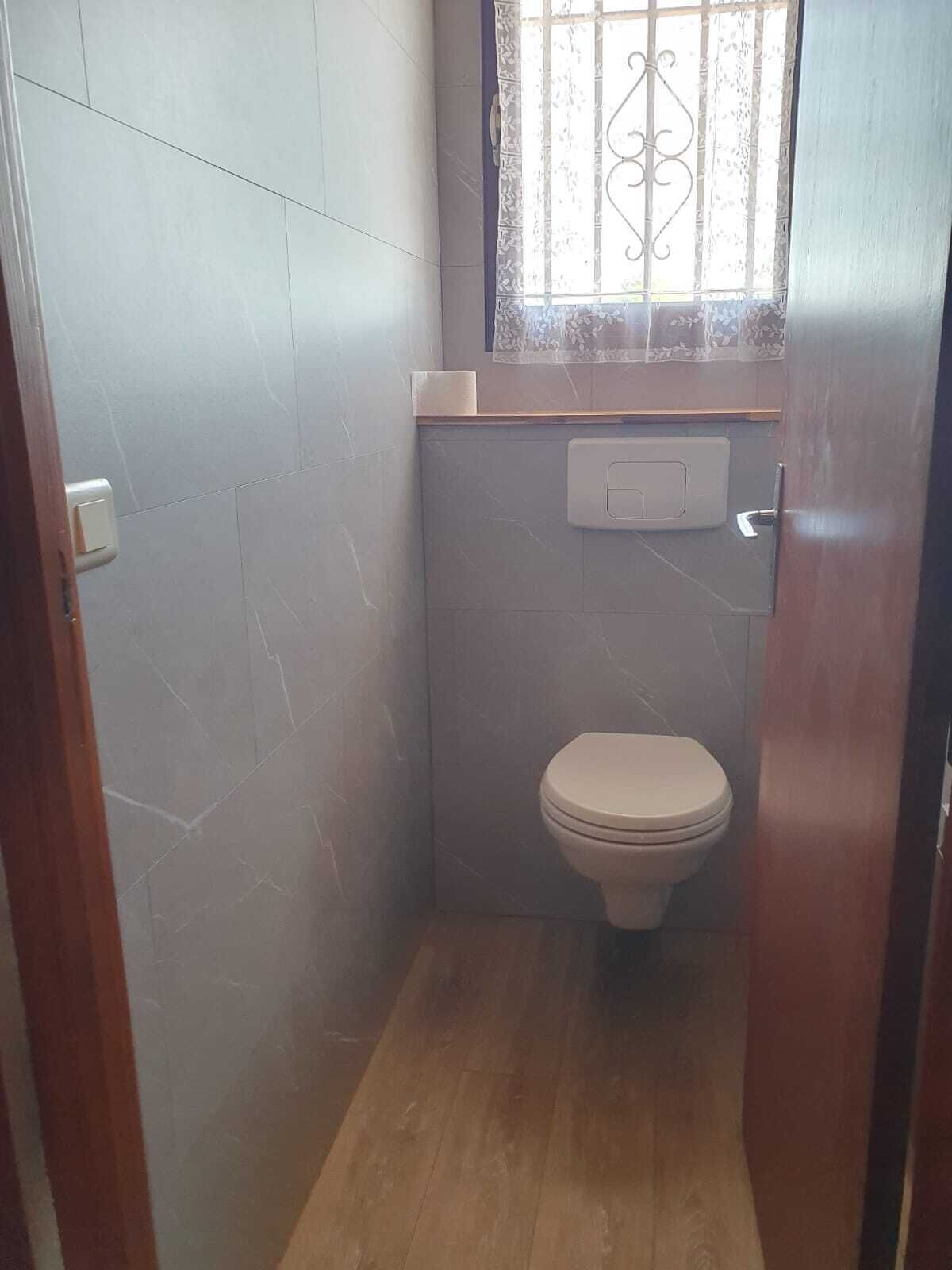 Une petite salle de bain avec des toilettes, une fenêtre ornée de barreaux décoratifs et un interrupteur sur le mur.