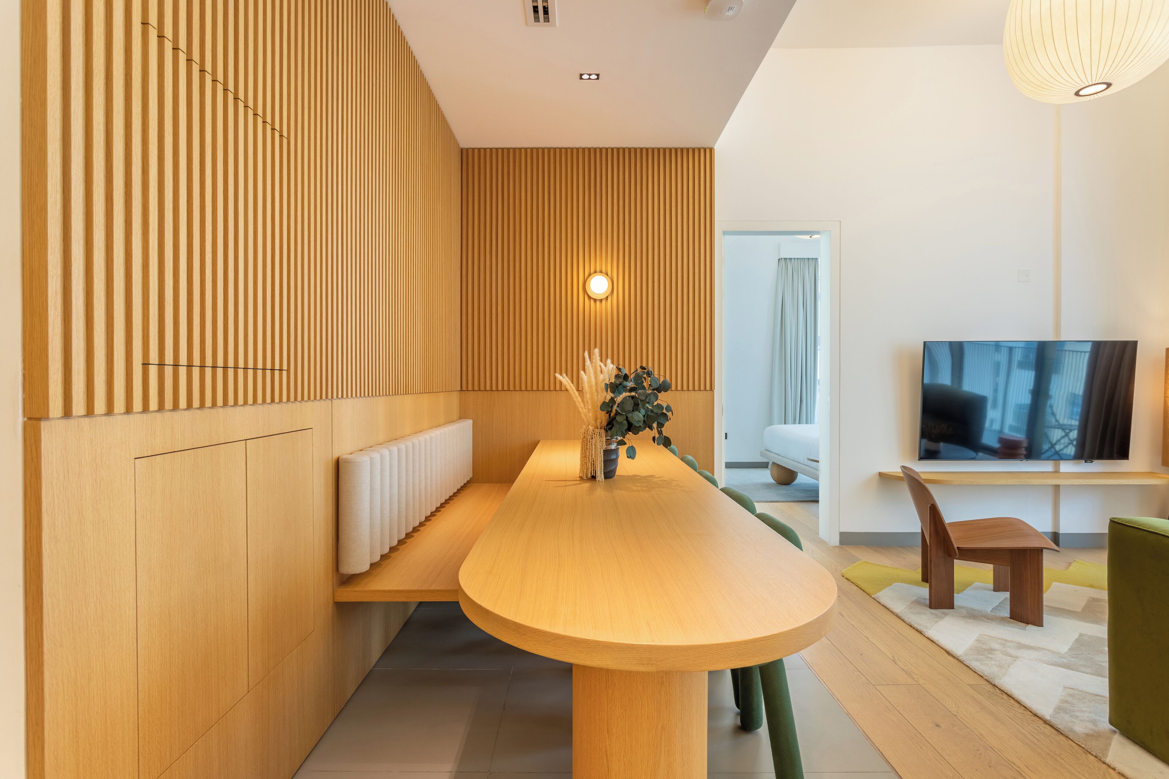 Un salon moderne avec un mur d’accent en bois, une table centrale en bois, un fauteuil vert et un téléviseur posé sur un meuble.