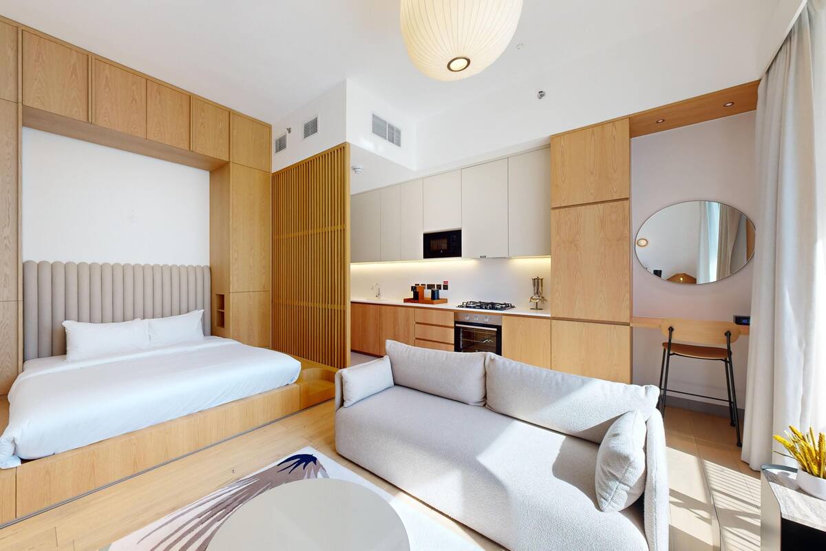 A modern hotel room with a bed, a sofa, a dining area, and a kitchen.