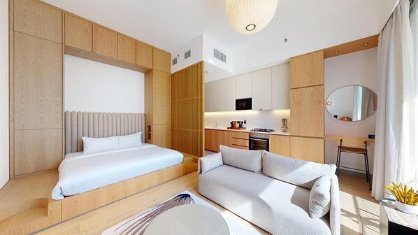 Ett modernt hotellrum med en säng, en soffa, en matplats och ett kök.