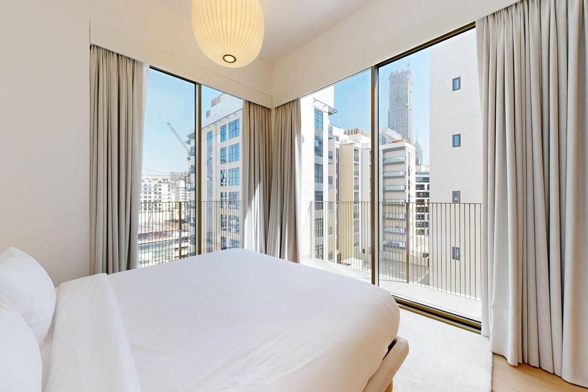 A modern hotel room with a large bed, a view of the cityscape, and a balcony with curtains.