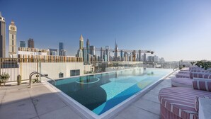 Ein Pool auf dem Dach mit Blick auf eine Stadtlandschaft, einer Glasbarriere und roten Liegestühlen.