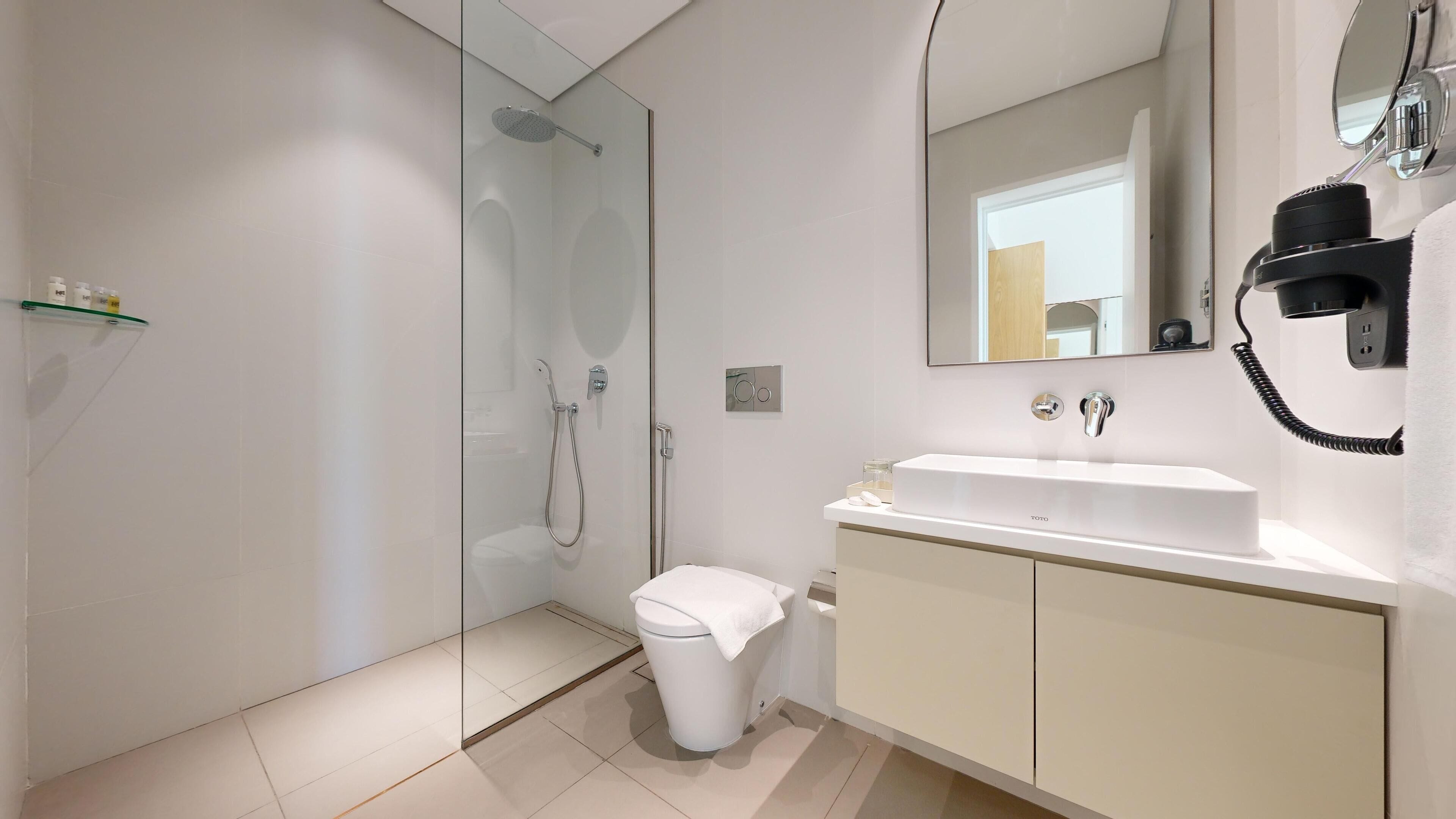 A modern bathroom with a glass-enclosed shower, a white toilet, and a white sink with a mirror above it.