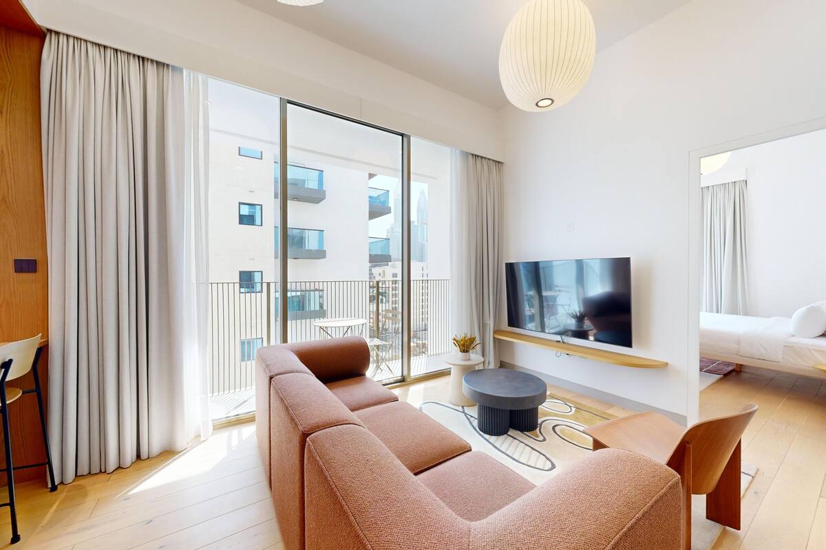 A modern living room with a sofa, a TV mounted on the wall, and a balcony with a view of the city.