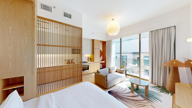 Ein Hotelzimmer mit einem großen Bett, einer Couch, einem kleinen Tisch, einem Balkon mit Blick und einer Küchenzeile.
