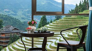 Una habitación con vistas a campos de arroz escalonados, un edificio tradicional y una mesa con una silla.