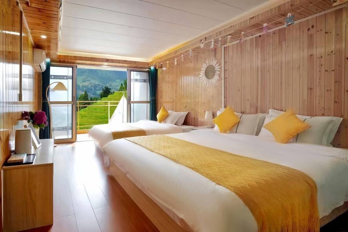 A bedroom with two beds, wooden walls, and a large window with a view of greenery.