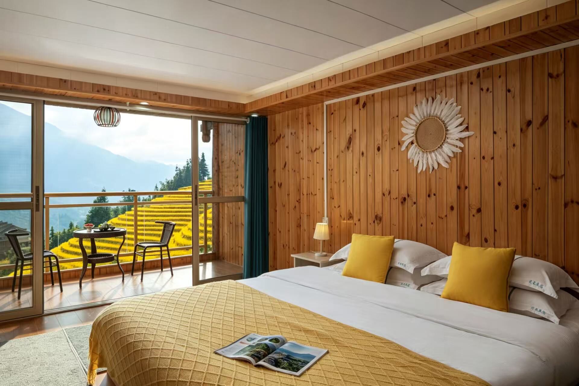 Un dormitorio con una cama grande, almohadas amarillas, una pared de madera, una decoración de sol y vistas a campos amarillos a través de una puerta de vidrio.