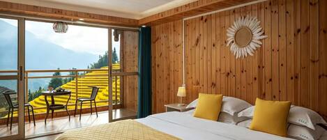 Un dormitorio con una cama grande, almohadas amarillas, una pared de madera, una decoración de sol y vistas a campos amarillos a través de una puerta de vidrio.