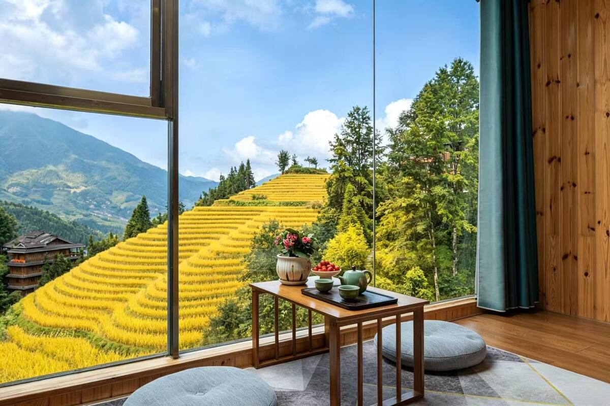 A room with a large window overlooking terraced fields and mountains.