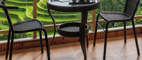 A balcony with a table and chairs overlooking terraced fields and mountains.