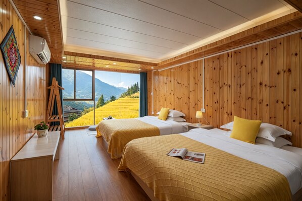 A hotel room with wooden walls, two beds with yellow bedding, a wooden bench, a small table with a plant, and a view of a mountain landscape.