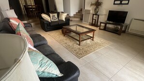 A living room with a sofa, coffee table, and TV. There is a staircase leading to another level. - Parry Suite (Weija)