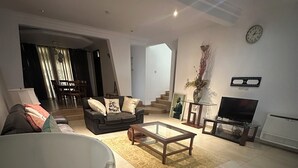 A modern living room with a sofa, a glass coffee table, a TV, and a staircase leading to another level. - Parry Suite (Weija)