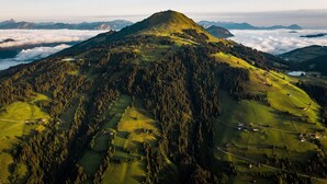 An aerial view of a mountain with a clear sky, surrounded by forested areas and a few scattered buildings. - Mountain & Golf Resort Westendorf (Westendorf)