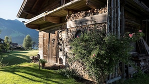 A rustic wooden house with a stone foundation, a wooden door, and a small garden with pink flowers. - Mountain & Golf Resort Westendorf (Westendorf)