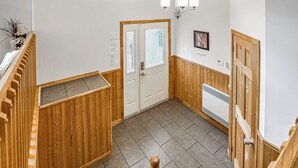 Um corredor com painéis de madeira, uma porta branca, um radiador e um candelabro.