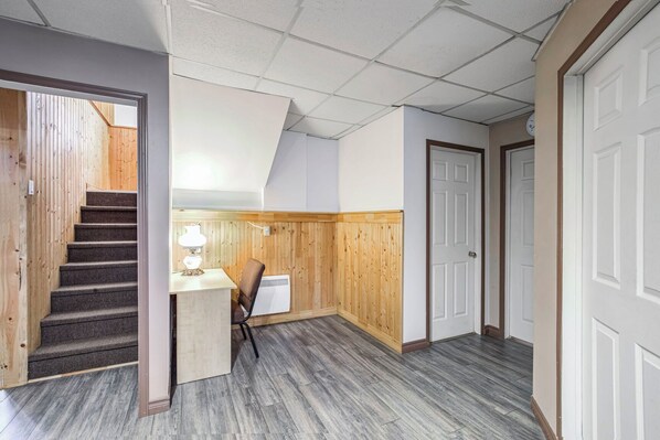 Un pasillo con una escalera de madera, un escritorio con una lámpara y una puerta blanca.
