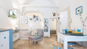 A cozy room with a white and blue color scheme, featuring a dining table set with blue and yellow plates, a blue chair, and a small stool. - Vico di Ostuni Apartments by Rentbeat (Ostuni)