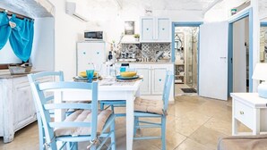 A bright kitchen with white and blue cabinetry, a dining table with chairs, and a visible door leading to another room. - Vico di Ostuni Apartments by Rentbeat (Ostuni)
