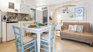 A compact kitchen with a dining area, a sofa, and a wall with decorative elements. - Vico di Ostuni Apartments by Rentbeat (Ostuni)